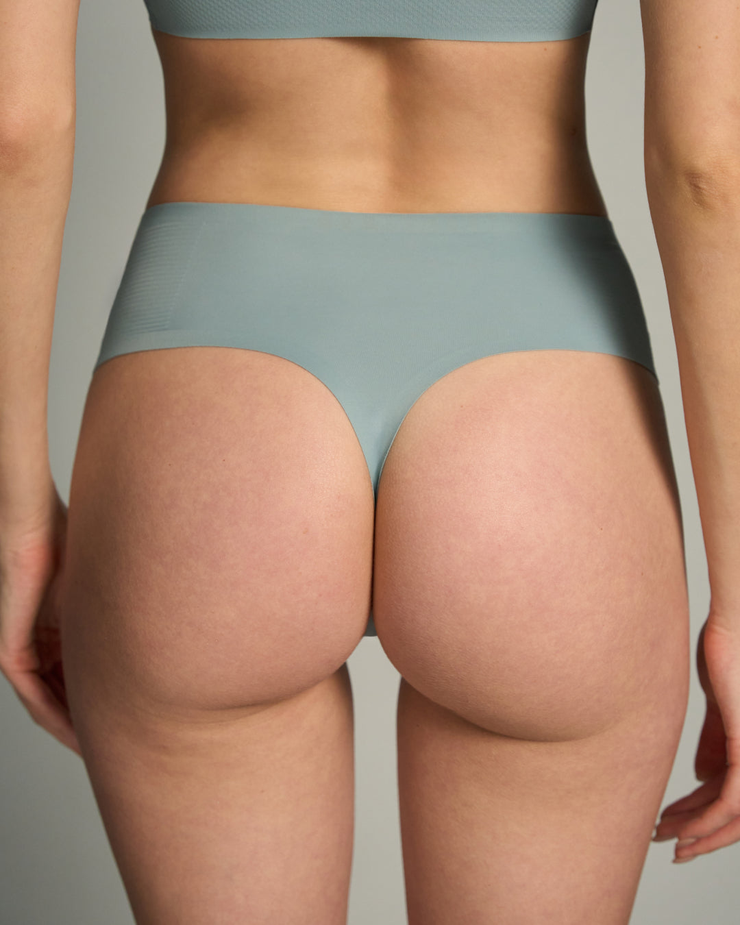 Person wearing  Arona Blue wireless bra and thong panty set against a neutral background