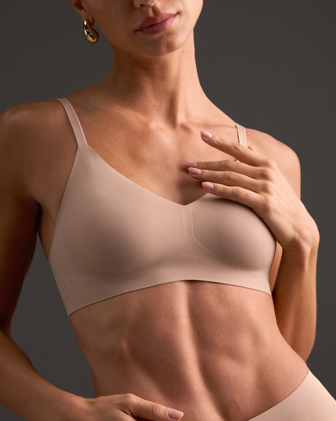 Woman wearing a  nude support  bralette against a dark background