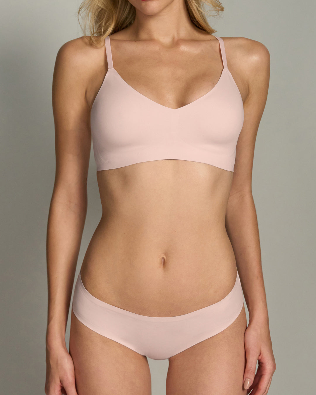 Model posing in light pink primrose bra and panty set against a neutral background