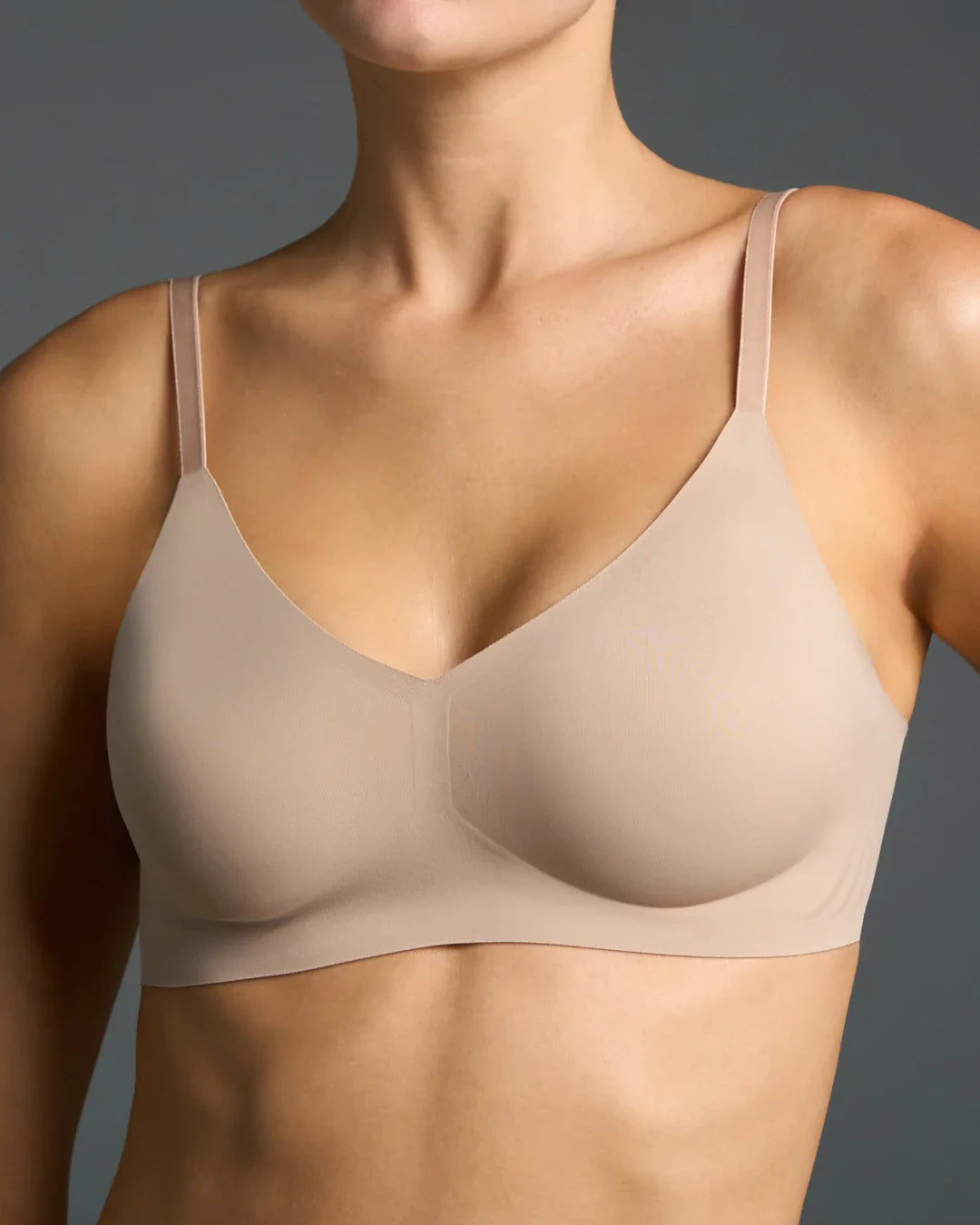 Seamless bralette in nude color with thin straps, modeled against a dark gray background